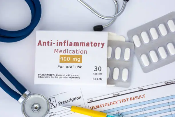 Anti-inflammatory medication or drug concept photo. On doctor table lies open packaging labeled "Anti-inflammatory" and fell out of her blisters with pills for treatment