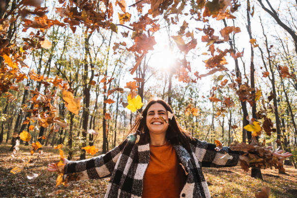 mujer lanzando hojas de otoño en la foto del parque - autumn leaf falling wind fotografías e imágenes de stock