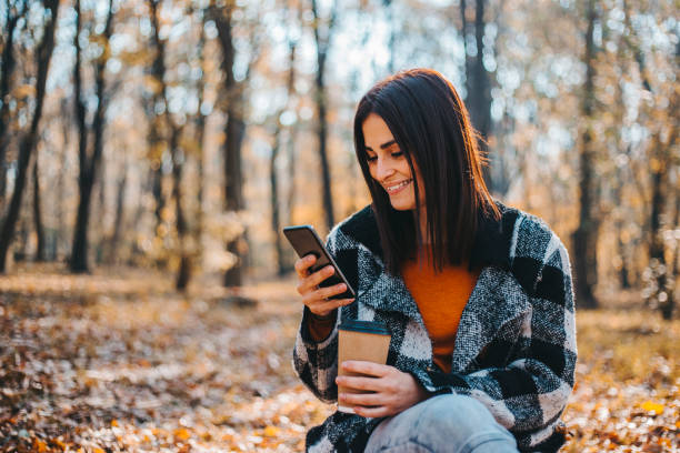 森の美しい秋の日にスマートフォンを使用して幸せな女性 - autumn women smiling leaf ストックフォトと画像