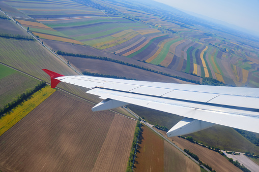 White airplane wing tilted in low flight over a crop fields pattern.