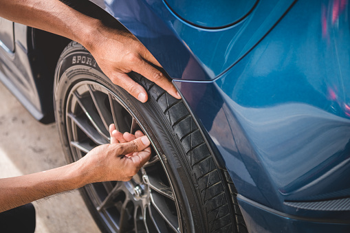 Closeup male automotive technician removing tire valve nitrogen cap for tire inflation service at garage or gas station. Car annual maintenance and repair concept. Safety road trip and travel theme.