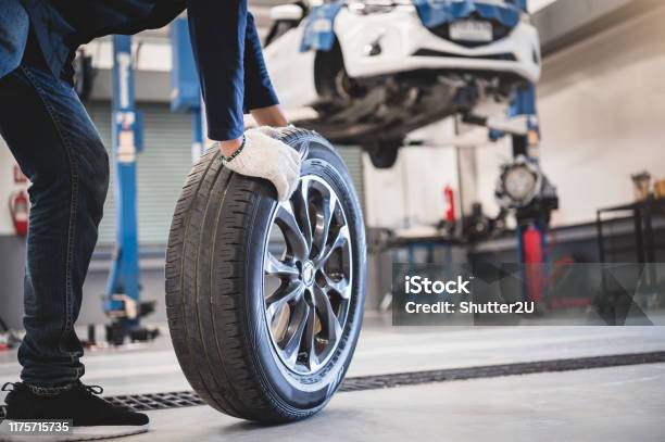Male Mechanic Hold And Rolling Tire At Repairing Service Garage Background Technician Man Replacing Winter And Summer Tyre For Safety Road Trip Transportation And Automotive Maintenance Concept Stock Photo - Download Image Now