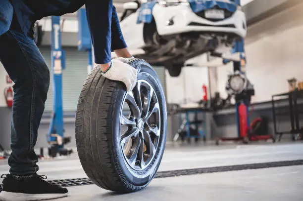 Photo of Male mechanic hold and rolling tire at repairing service garage background. Technician man replacing winter and summer tyre for safety road trip. Transportation and automotive maintenance concept