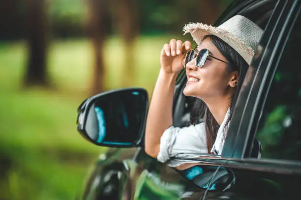 Photo of Happy woman hand holding hat outside open window car with meadow and mountain lake background. People lifestyle relaxing as traveler on road trip in holiday vacation. Transportation and travel concept