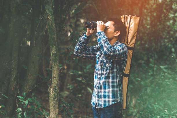 istock Man with binoculars telescope in forest looking destination as lost people or foreseeable future. People lifestyles and leisure activity concept. Nature and backpacker traveling jungle background 1175716290