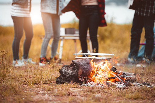 Closeup of campfire with friendship dancing to beat of the music for celebrating in party with mountain meadow and lake view background. People lifestyle and travel vacation. Picnic and camping tent