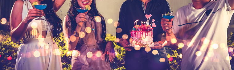 Closeup lower body friends group having outdoor birthday party at night club with birthday cake. Event and anniversary concept. People lifestyles and friendship forever in night club banner background