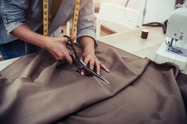 dressmaker cutting dress fabric on sketch line with sewing machine. fashion designer tailor or sewer in workshop studio designing new collection clothes. business owner shop and entrepreneur concept - dressmakers model fotos imagens e fotografias de stock