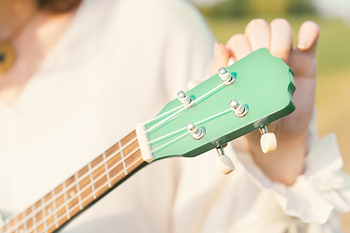 Woman tuning ukulele strings. The fretboard of the musical instrument is mint color. Fashionable shades of green