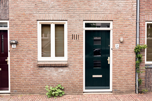 Deventer / The Netherlands - July 2019: View of a characteristic brick house front / facade with wooden doors with lintel panels, flower gardens in the center of Deventer, The Netherlands.
