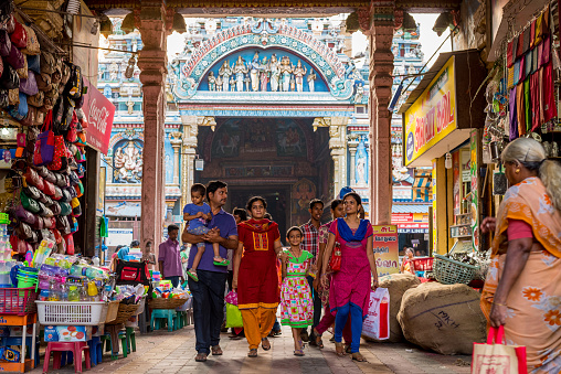 Madurai, Tamil Nadu / India - January 14, 2016: an Indian family walks through an arch occupied by shops, with famous Meenakshi Temple (also known as Meenakshi Amman or Meenakshi-Sundareshwara Temple) in the background. The temple is the main tourist attraction of the city.