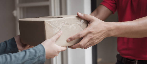 istock Panoramic banner. delivery service man in red uniform with woman customer receiving parcel post box from courier at home, cargo shipping, express delivery service, online shopping and logistic concept 1175728026