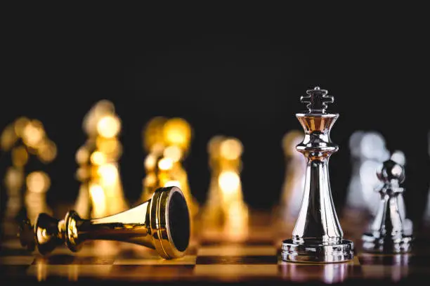 Closeup king chess piece defeated enemy or trade competitor by checkmate at end of chessboard game. Businessman moving chess to success competition by hand. Leadership and strategy management