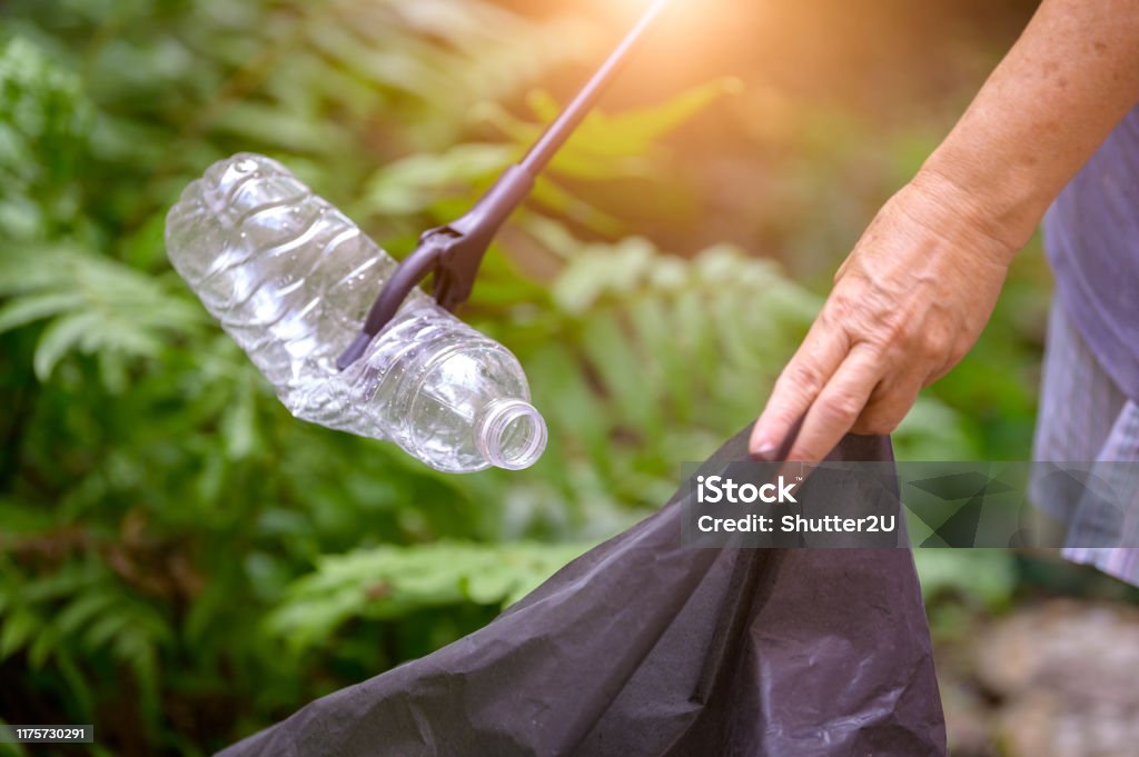 Closeup of hand and waste grabber picking up drinking plastic bottle waste into bag. Ecology and Environmental concerns. Recycling waste reduction techniques. Eco-friendly earth world disaster relief. Garbage Stock Photo