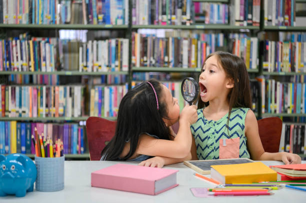 две маленькие счастливые милые девушки делают смешное лицо и играть вместе в библиотеке в школе, как стоматологическая проверка здоровья. � - humor book fun human age стоковые фото и изображения