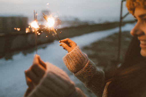 Happy woman holding sparklers while enjoying in a winter day on the rooftop