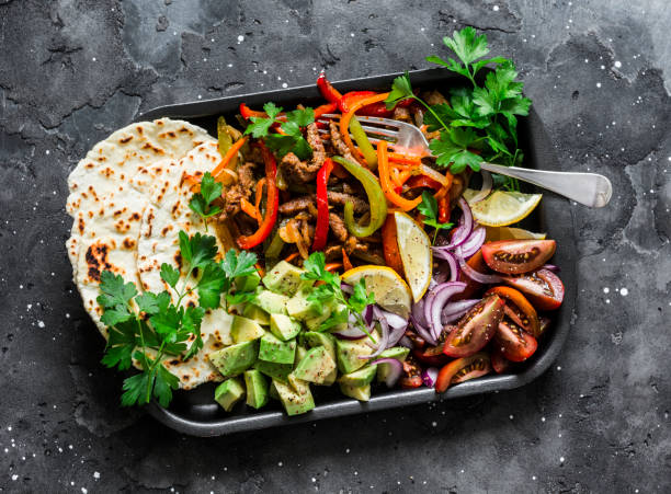 Spicy beef, vegetables, avocado, corn tortillas fajitas on a sheet pan on a dark background, top view. Delicious snack, tapas in mexican style Spicy beef, vegetables, avocado, corn tortillas fajitas on a sheet pan on a dark background, top view. Delicious snack, tapas in mexican style fajita photos stock pictures, royalty-free photos & images