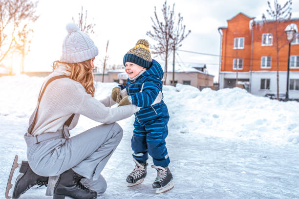 mamá con niño de 3-5 años de edad, aprender a entrenar, montar en la ciudad de invierno en la pista, patinaje sobre hielo. niños felices sonrientes juegan divirtiéndose fin de semana primeros pasos patinaje sobre hielo infantil. espacio libre para tex - sports and fitness flash fotografías e imágenes de stock