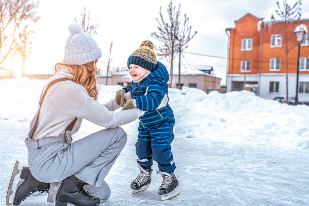 mom with baby boy 3-5 years old, learn to train, ride in winter city on rink, ice skating. happy smiling children play having fun weekend weekend first steps child ice skating. free space for text. - happy kid flash imagens e fotografias de stock