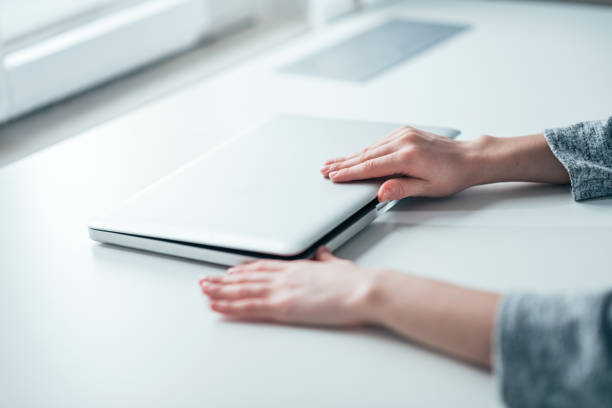 Businesswoman's hands closing or opening laptop on white table in bright office.