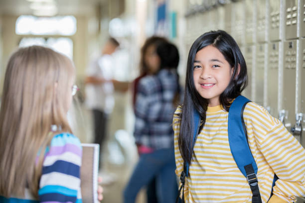 istock Junior high student smiles in hallway near lockers while talking to friend 1175745993