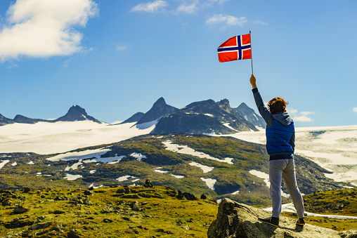 Tourist woman enjoy mountains landscape, holding norwegian flag. National tourist scenic route 55 Sognefjellet, Norway