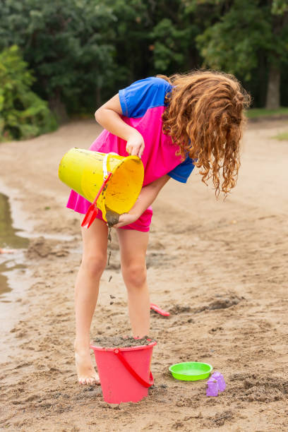 istock Girl Pouring Sand From Bucket While Playing on Beach 1175763719