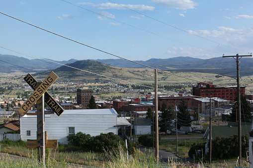 The older uptown district of Butte, Montana is viewed from a grassy hillside with a trail crossing sign in the foreground.