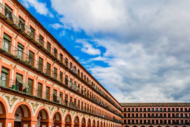 The Plaza de la Corredera with its windows, balconies and arches with a combination of brown and orange colors with a blue sky and white clouds in Cordoba Spain