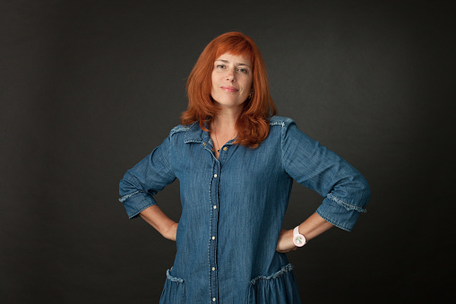 Studio portrait of a 50 year old attractive red-haired woman in a blue dress on a black background