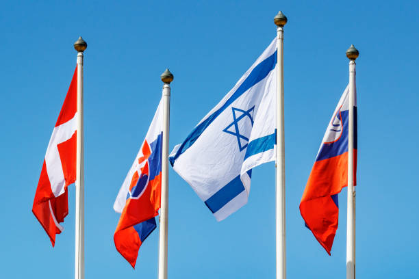 istock Flags of different countries waves on the wind on flagpole against blue sky in sunlight 1175780693