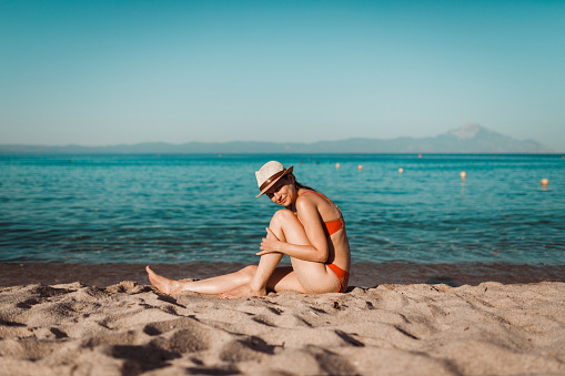 Young woman sitting at the sandy beach and enjoying the view on a sunny summer day in Greece