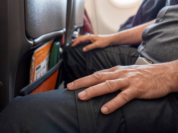 un homme reposant ses mains sur ses genoux pendant qu'il s'assied à bord d'un vol commercial - travel buckle part of on top of photos et images de collection