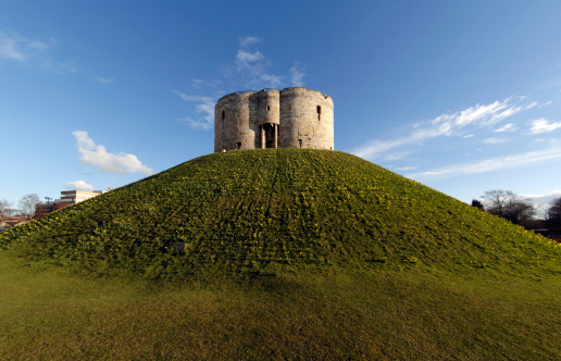 Cliffords Tower in York, UK, the site where in 1190 AD 150 jews committed suicide rather than face an angry mob outside, some setting fire to themselves. Fisheye view and distortion corrected. Focus entirely on tower and falling off away from tower. Shot taken in Spring and daffodils cover the mound.