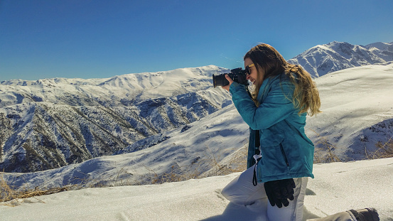 Side view of a brazilian woman wearing ski clothes photographing a snowy landscape in Farellones/Chile.