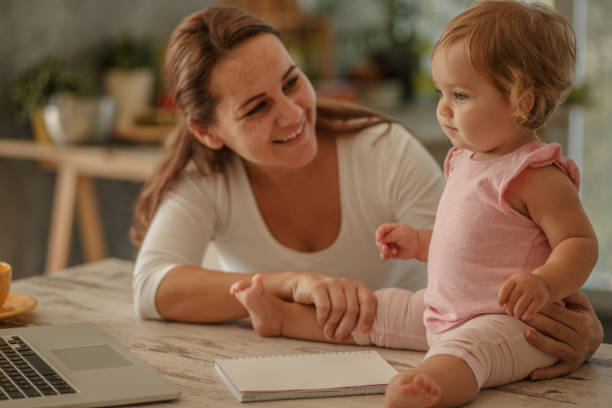 istock Cheerful mother playing with her cute baby daughter while using laptop 1175802561