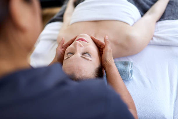 mujer china masajista terapeuta dando un tratamiento a un cliente rubio atractivo en la mesa de masaje en un consultorio médico brillante - massage therapist massaging sport spa treatment fotografías e imágenes de stock