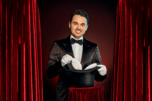 istock Professional Occupation. Magician in suit and gloves standing isolated on wall making trick taking bunny from hat on table smiling happy 1175803464