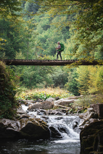 Woman hiking in nature, she walking on footbridge over beautiful river in mountain.
