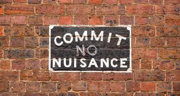 A 'Commit No Nuisance' street sign painted onto a brick wall in a city back alleyway