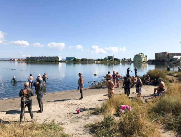 A lot of people visit the lake where they are doing mud treatments Pomorie, Bulgaria - September 08, 2019: People visit Lake Pomorie. It is an ultrasaline natural lagoon which is also the northernmost lake of the Burgas Lake Group. pomorie stock pictures, royalty-free photos & images