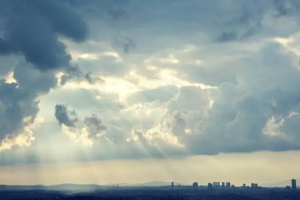 Cityscape with thick clouds and sunbeams shining through.