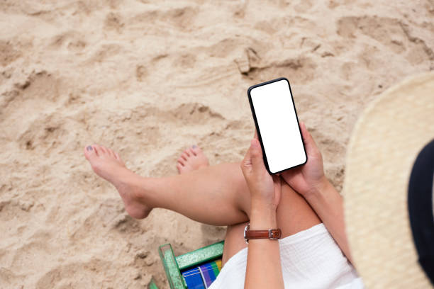 istock a woman holding black mobile phone with blank desktop screen while sitting on a beach chair 1175838810