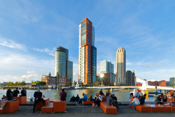 Rotterdam, Netherlands - September 15, 2019: The new harbor district of Rotterdam (Kop van Zuid) located on the south bank of the Nieuwe Maas, opposite to the city center of Rotterdam. The Hotel New York (old building on the left) is situated in the former head office of the Holland America Line. Montevideo residential house in the centre. A lot of people enjoy the warm late summer afternoon.