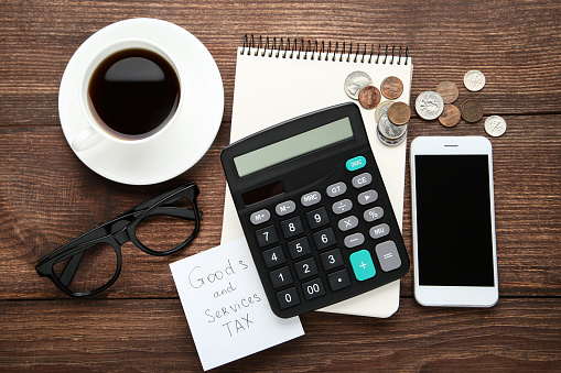 Inscription Goods and Services Tax with coins, banknotes, calculator, smartphone and cup of coffee