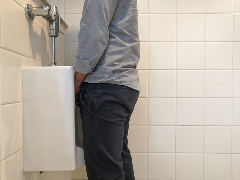 Businessman holding his crotch in front of a toilet and a pile of toilet paper rolls isolated on white background