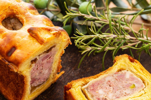 Pate in croute or pie with rosemary twig and green olives on branch with leaves over a dark wooden cutting board and a used oak wood background. stock photo