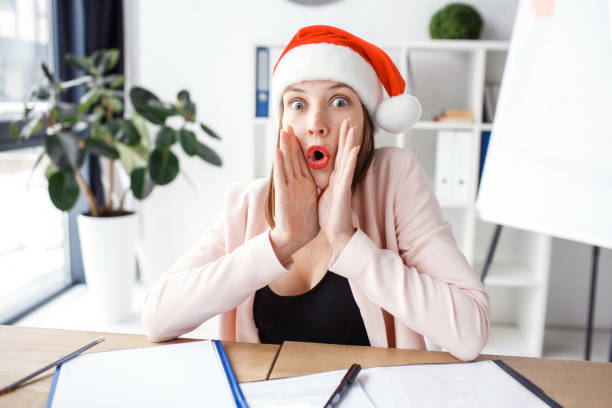 istock Amazed beautiful young woman whispering. Sit at table in office and look scared on camera. Alone in room. Festive look. Celebrating new year or Christmas. 1175853123