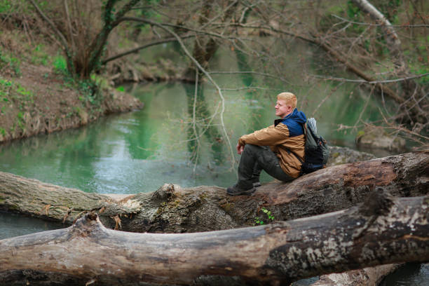 istock Man sits on a log by the green river 1175854354