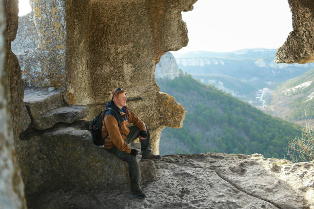 istock Man sits on stone steps in cave with huge hole in the wall in Crimea 1175854462